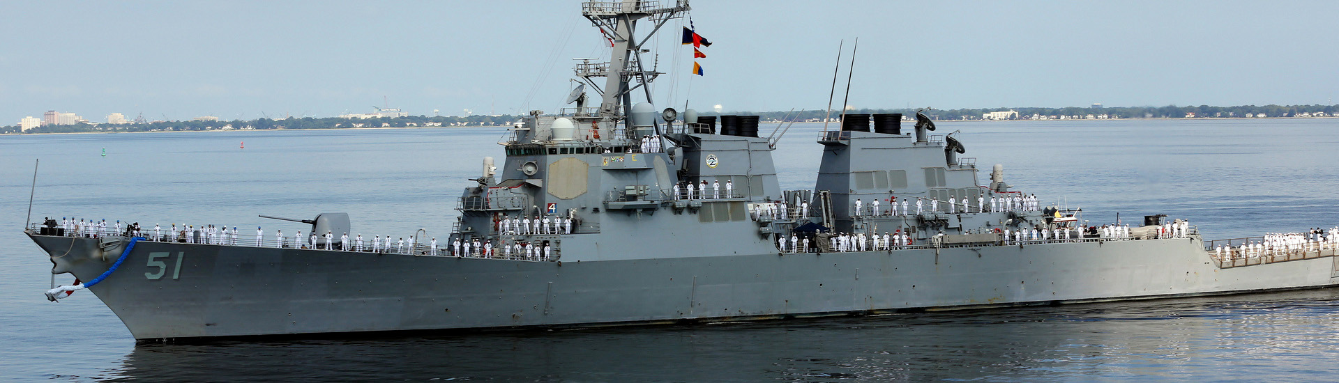 Navy ship with sailors on deck leaving port.
