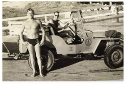 Black and white photo of two young men, one standing in swimsuit, another in vehicle.